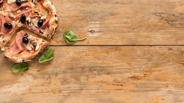 Vue de dessus de délicieuses pizzas avec feuille de basilic sur un bureau en bois