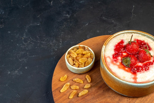 Vue de dessus d'un délicieux petit-déjeuner servi avec de la confiture de fraises dans un bol et des pointes de raisins secs jaunes sur une planche de bois ronde sur le côté gauche sur fond de couleur sombre