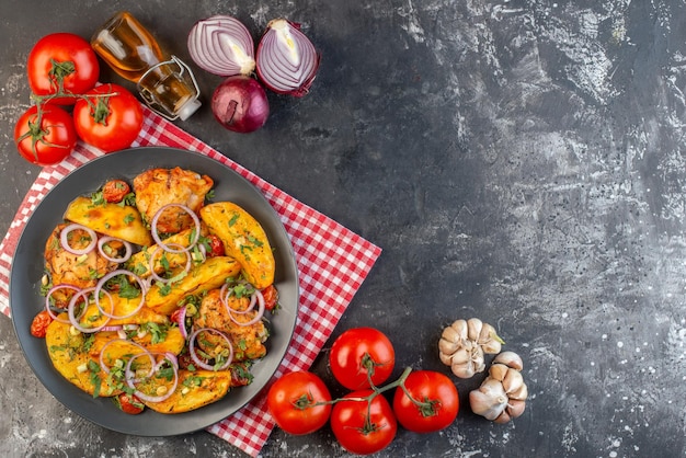 Vue de dessus d'un délicieux repas de poulet avec des pommes de terre et des légumes verts sur une serviette pliée rouge dépouillée de légumes épices bouteille d'huile tombée sur une table de couleur foncée