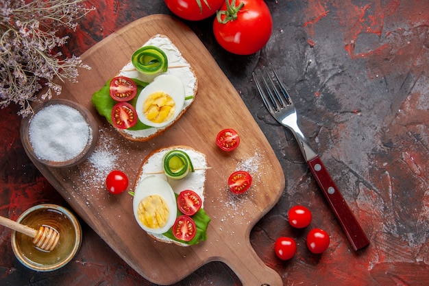 vue de dessus de délicieux sandwichs aux œufs avec des tomates rouges sur une planche à découper fond rouge foncé déjeuner sandwich nourriture repas collation toast pain burger