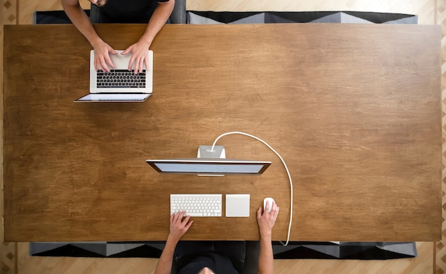 Vue de dessus de deux hommes travaillant sur leurs ordinateurs à une table de travail en bois vide. Espace copie de travail indépendant à plat.