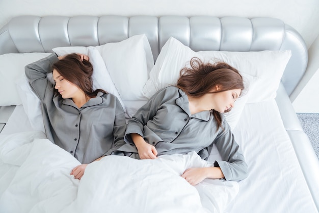 Vue de dessus de deux jolies jeunes sœurs jumelles dormant dans leur lit