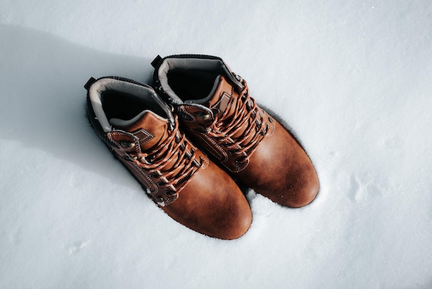 Vue de dessus de deux nouvelles bottes d'hiver marron en cuir pour hommes debout dans la neige par une journée ensoleillée, à l'extérieur. Chaussures de randonnée et de voyage. Élément de vêtement, pas de personnes.