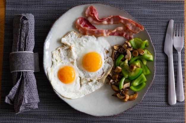 Vue de dessus de deux œufs au plat avec bacon, poivrons verts et champignons