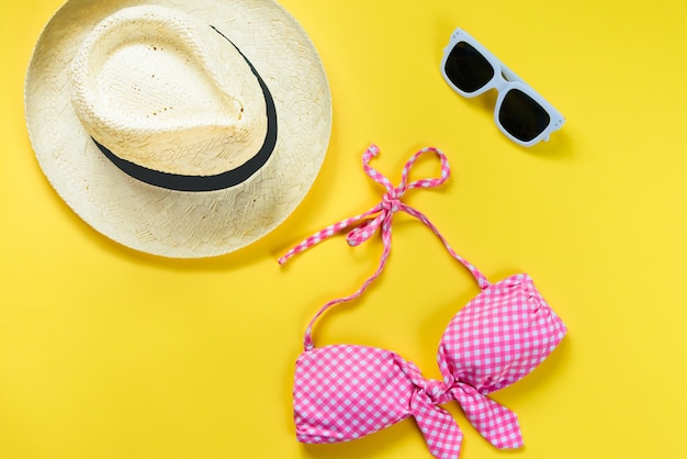 Vue de dessus de deux pièces rose maillot de bain à carreaux, lunettes de soleil blanches et chapeau de paille sur jaune