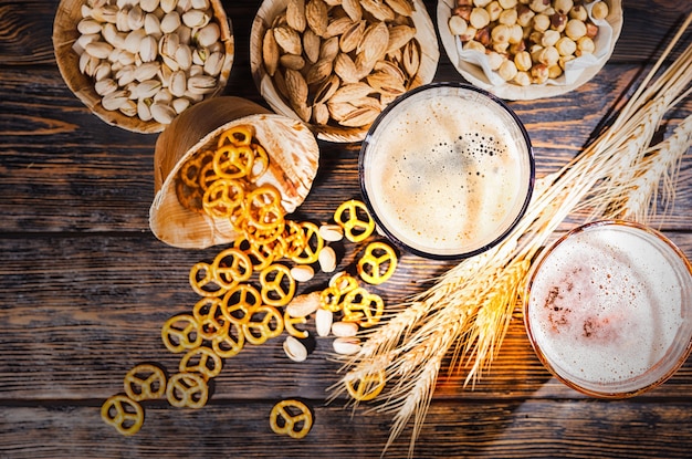 Vue de dessus de deux verres avec de la bière foncée et légère fraîchement versée près du blé, éparpillés de petits bretzels et pistaches sur un bureau en bois foncé. Concept de nourriture et de boissons