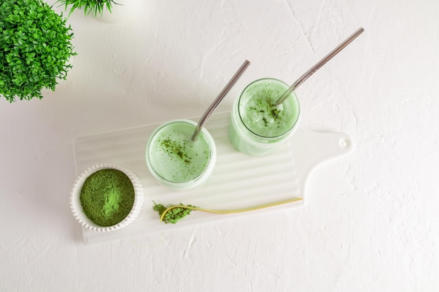 Vue de dessus de deux verres en verre avec de la paille et du thé matcha latte naturel fraîchement préparé fond blanc nettoyant améliorant le métabolisme