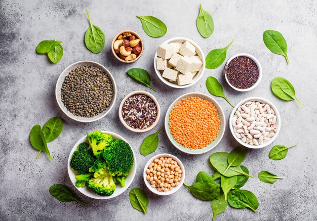 Vue de dessus de différentes sources de protéines végétaliennes : haricots, lentilles, quinoa, tofu, légumes, épinards, noix, pois chiches, riz, fond rustique en pierre. Une alimentation végétarienne saine et équilibrée pour les végétaliens