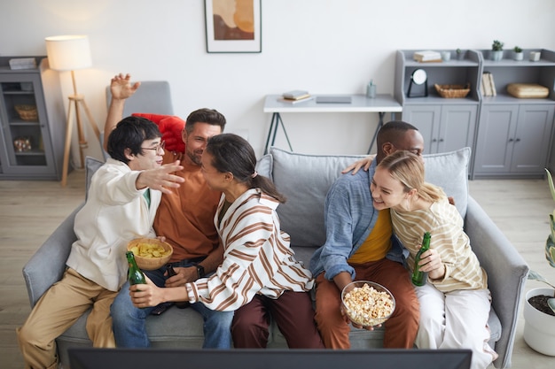 Vue de dessus à divers groupes d'amis s'embrassant tout en regardant des films ensemble à la maison