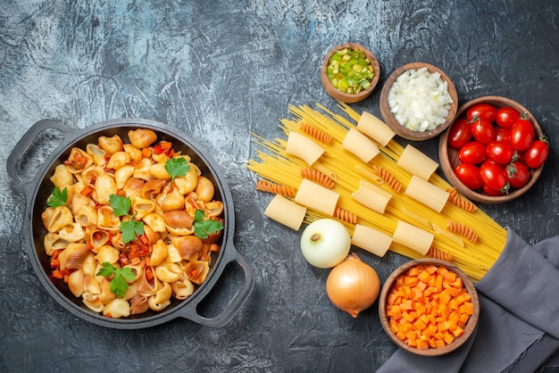 vue de dessus diverses pâtes rigatoni spaghetti spirales légumes hachés dans des bols pâtes savoureuses dans une poêle à frire sur fond gris