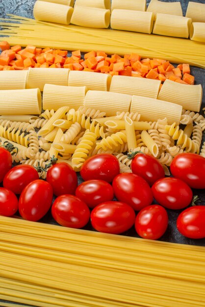 vue de dessus diverses pâtes spaghetti penne spirales tomates cerises carottes hachées sur fond gris