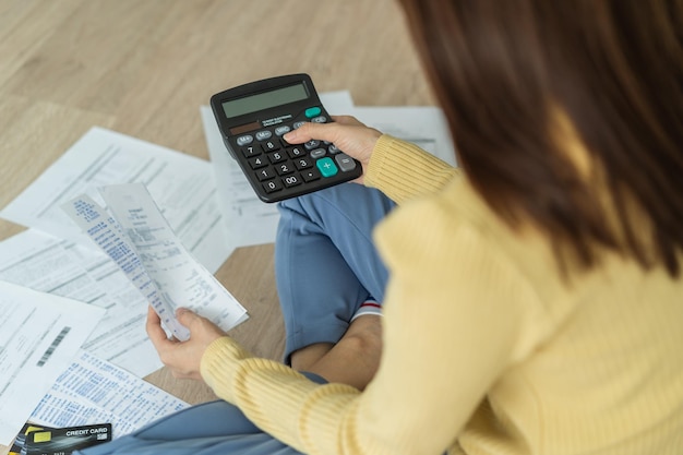 La vue de dessus doit une femme asiatique, une femme assise sur le sol stressée et confuse en calculant les dépenses à partir d'une facture ou d'une facture, n'a pas d'argent à payer, une hypothèque ou un prêt. Concept de dette, de faillite ou de faillite.