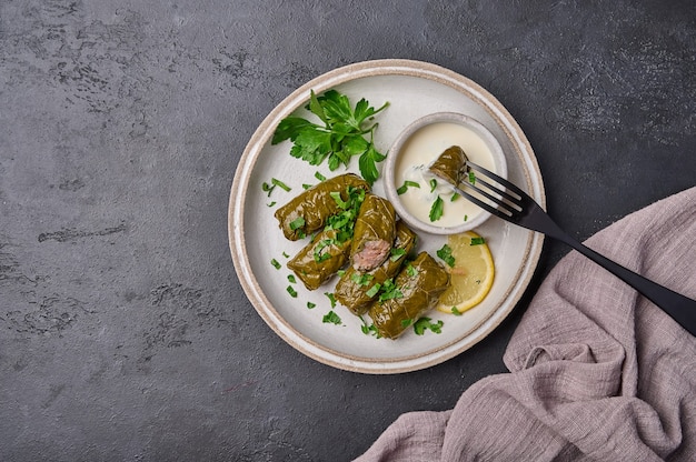 Vue de dessus dolma avec persil et citron dans une assiette légère avec de la crème sure sur une fourchette noire piquée