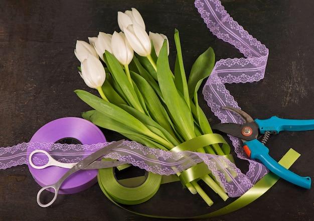 Vue de dessus du beau bouquet de tulipes dans du papier d'emballage, des rubans et de vieux ciseaux sur une table en bois