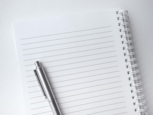 Vue de dessus du blanc vide de la page du cahier Modèle de feuille de papier blanc avec ligne pour note de mémo sur le bloc-notes à spirale verticale avec un stylo argenté isolé sur fond de cuir de luxe blanc