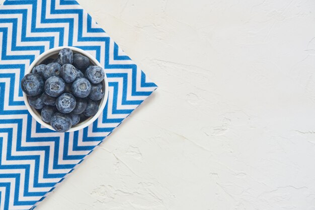 Vue de dessus du bol avec des bleuets sur textile bleu et béton blanc