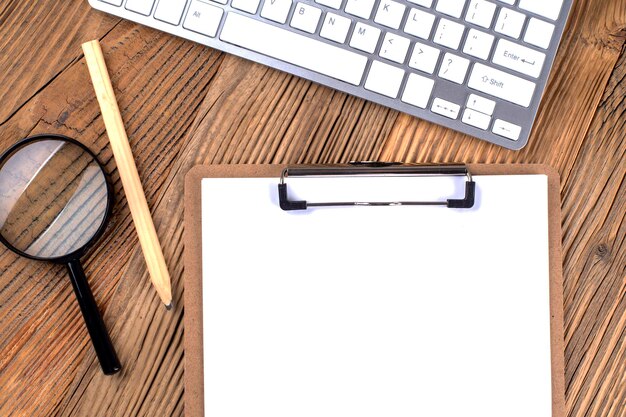 Photo vue de dessus du bureau agencement de bureau avec clavier loupe et presse-papiers avec papier vierge sur le fond en bois vue de dessus espace de copie