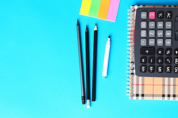 Vue de dessus du bureau bleu avec des crayons, une calculatrice et un cahier. Retour au concept d&#39;école.