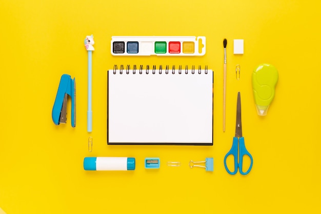 Vue de dessus du bureau moderne blanc, bleu, jaune avec fournitures scolaires et papeterie sur table autour d'un espace vide pour le texte. Retour au concept de l'école à plat avec maquette