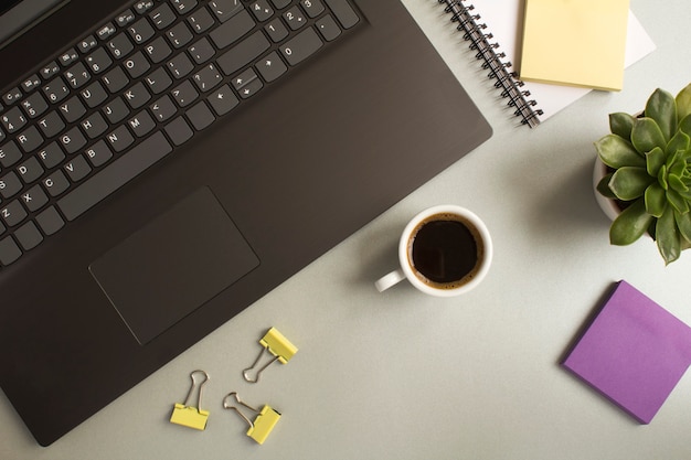 Vue de dessus du bureau avec ordinateur portable, tasse à café, cactus et articles de papeterie sur la table grise. Mise à plat du bureau de l'espace de travail.