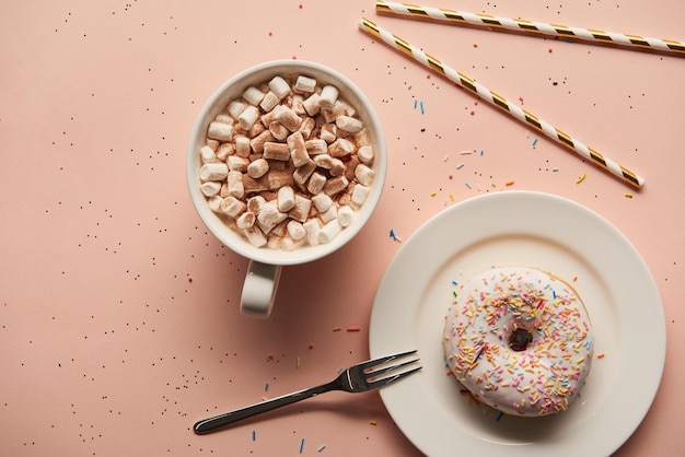 Vue de dessus du cacao sucré avec des guimauves près du beignet sur fond rose