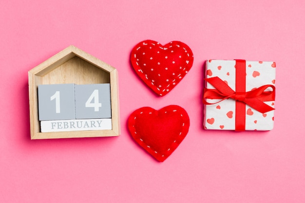 Vue de dessus du calendrier en bois, des coffrets cadeaux blancs et des coeurs en textile rouge sur coloré. La Saint-Valentin