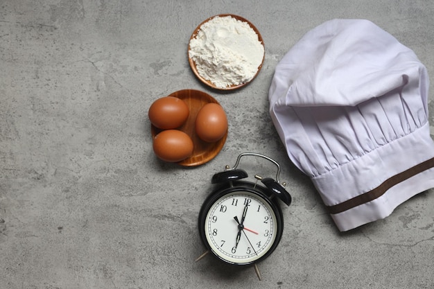 Vue de dessus du chapeau de chef avec ingrédients de cuisine et réveil sur fond rustique gris