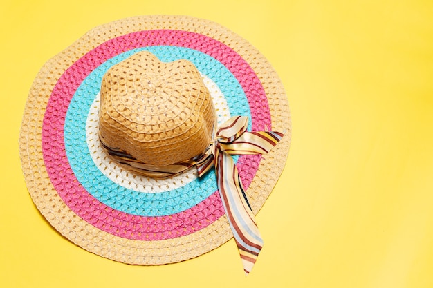 vue de dessus du chapeau d'été pour femmes avec un nœud en ruban et des lignes de couleurs blanches, roses et bleues sur jaune.