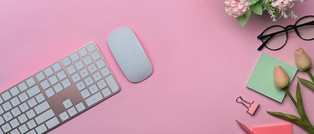 Vue de dessus du clavier sans fil, des notes autocollantes et des lunettes sur fond rose.