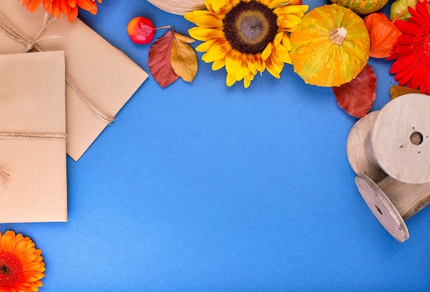 Vue de dessus du coffret cadeau artisanal, fleurs jaunes et orange et citrouilles sur fond bleu. Carte de voeux vierge pour le travail créatif. mise à plat