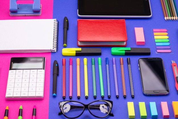 Vue de dessus du composite de bureau d'affaires avec smartphone, calculatrice, autocollants et stylos colorés sur rose et bleu