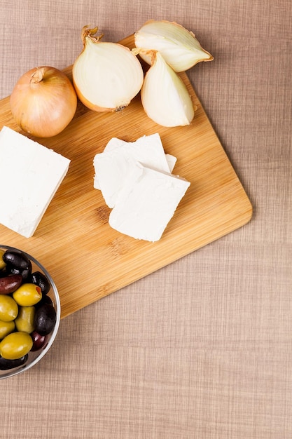 Vue de dessus du fromage feta blanc sur une planche de bois sur une table avec des olives et des oignons coupés