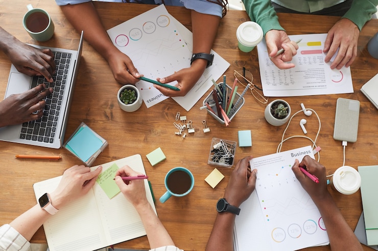 Photo vue de dessus du groupe multiethnique de personnes travaillant ensemble à une table en bois encombrée avec des tasses à café, des tasses et des articles de papeterie, le travail d'équipe ou l'étude du concept