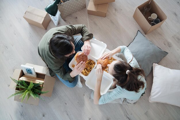 Vue de dessus du jeune couple avec des hamburgers et des boîtes se déplaçant dans un nouvel appartement