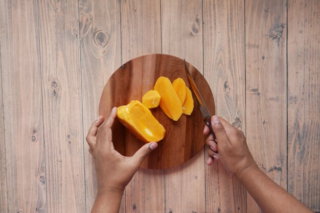 Vue de dessus du jeune homme main coupant la mangue sur une planche à découper