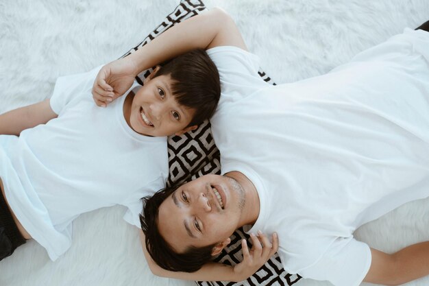 Vue de dessus du jeune père asiatique en fils mignon en chemise blanche allongé sur le lit avec une expression souriante s