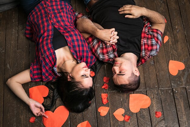 Vue de dessus du joli couple de la Saint-Valentin se regardant avec un coeur rouge dans les mains sur le fond en bois et les coeurs en papier. Homme et femme passionnés sur le sol. jour d'amour