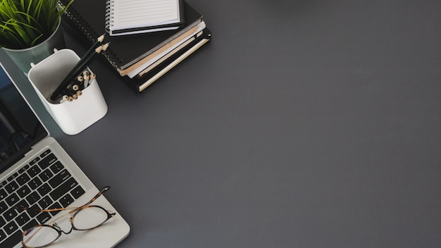 Vue de dessus du lieu de travail moderne avec ordinateur portable et fournitures de bureau sur table sombre