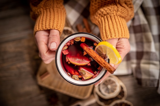 Vue de dessus du mug avec du vin chaud rouge détenu par une femme en pull tricoté