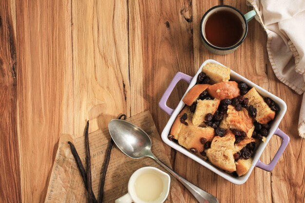 Vue de dessus du pain aux raisins et de la cannelle à la vanille et du pudding au beurre sur un plat de cuisson carré avec espace de copie pour le texte. Sur Table En Bois.