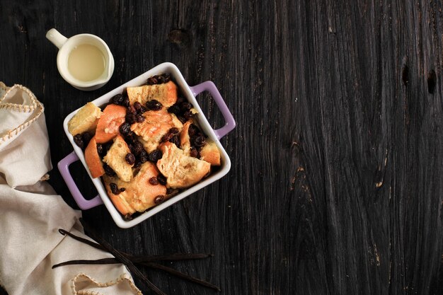 Vue de dessus du pain aux raisins et de la cannelle à la vanille et du pudding au beurre sur un plat de cuisson carré avec espace de copie pour le texte. Sur Table En Bois.