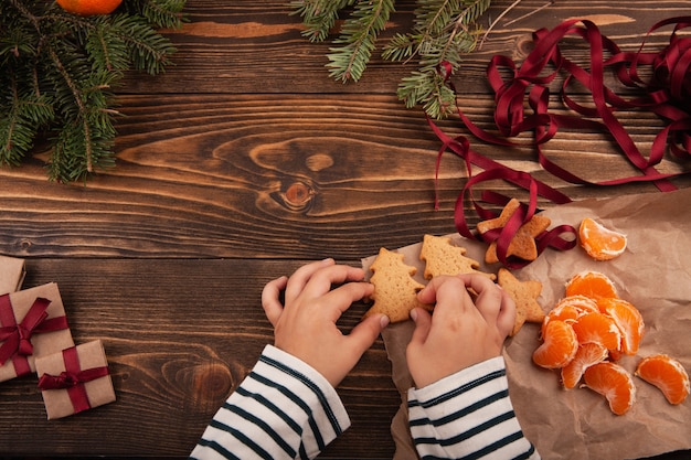 Vue de dessus du petit enfant assis à la table et tenant des biscuits de Noël dans ses mains.