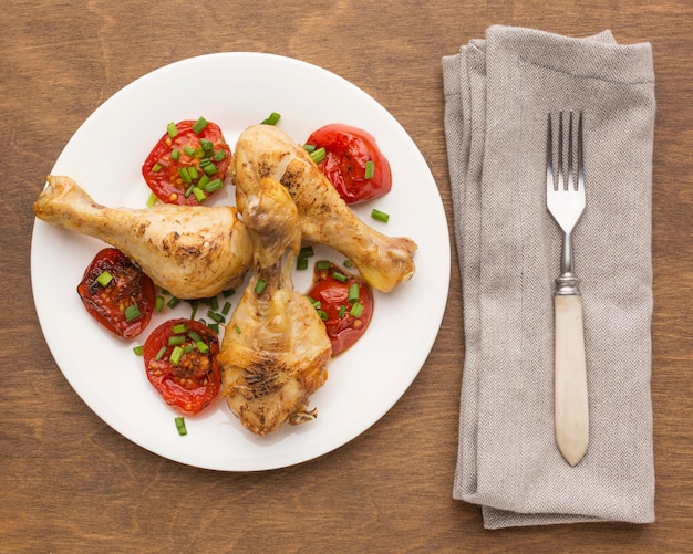 Vue de dessus du poulet et des tomates cuits au four sur une assiette avec une fourchette et un torchon