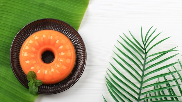 Vue de dessus du pudding à la mangue et à l'orange sur une plaque noire avec une feuille de menthe sur une table en bois