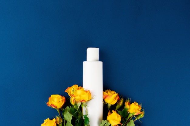 Vue de dessus du récipient cosmétique blanc avec des fleurs sur fond bleu, copie espace