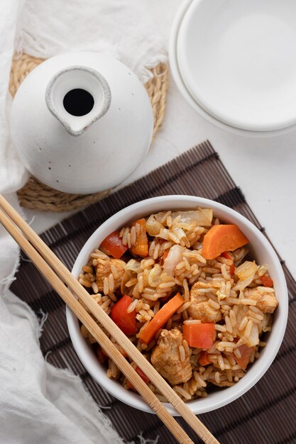 Vue de dessus du riz au poulet et aux légumes servi dans un bol blanc avec des baguettes Fond blanc