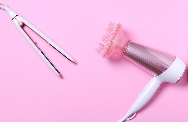 Vue de dessus du sèche-cheveux blanc et rose et fer à lisser sur rose. Mise à plat, minimalisme.Concept de soins capillaires.Outil de coiffure professionnel ionique rose métallique.