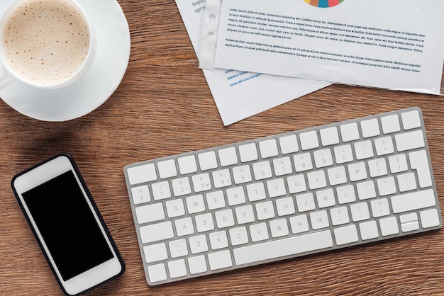 Vue de dessus du smartphone à clavier avec écran blanc et tasse à café sur fond en bois