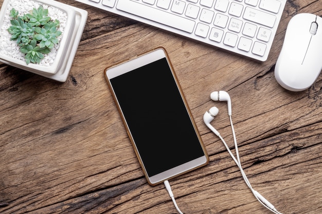 Vue de dessus du smartphone vierge, écouteurs, clavier et souris sur le bureau en bois grunge.