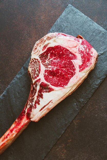 Vue de dessus du steak de boeuf cru en marbre séché Tomahawk sur un papier kraft avec des épices Concept de cuisine à plat